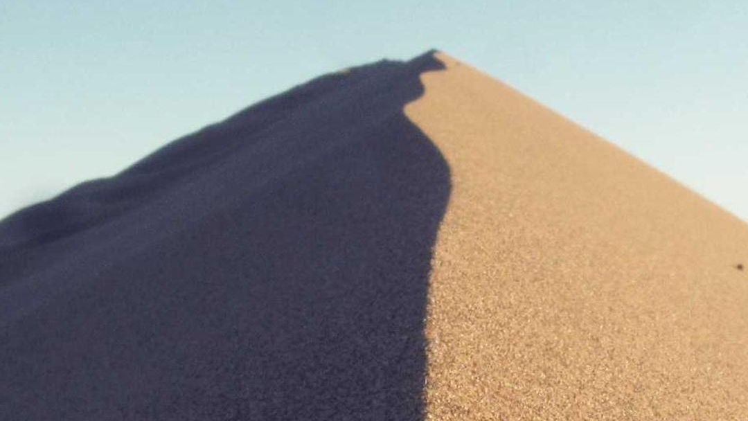 The sharp ridge of a sand dune against a pale sky