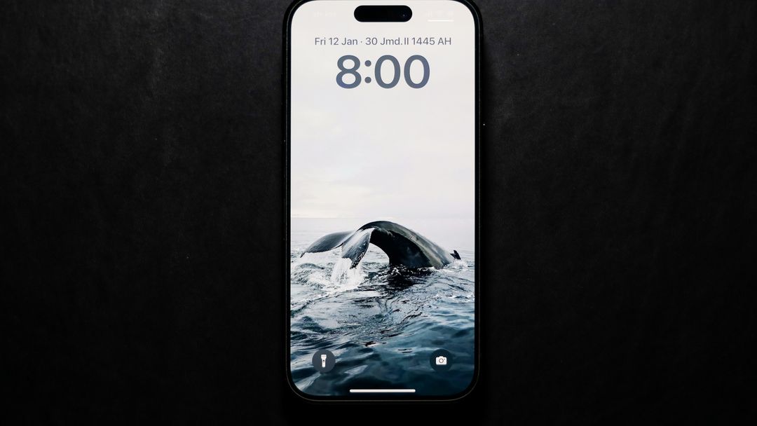 An iPhone on a dark surface, its Lock Screen showing a whale's tail rising from the sea under the clock