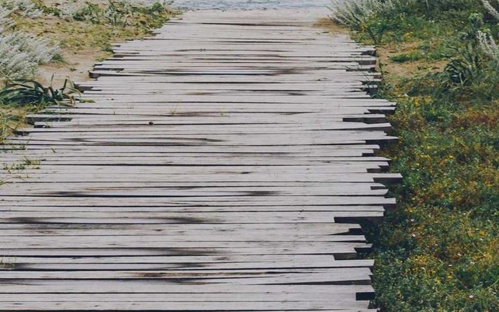A wooden boardwalk through dune grass toward the sea